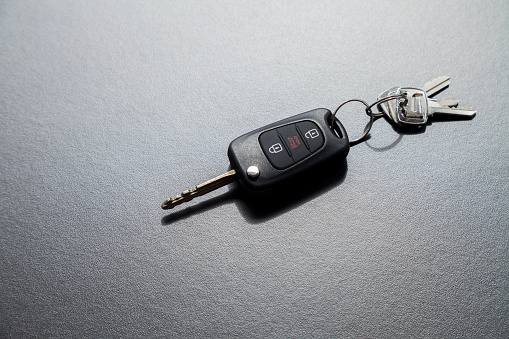 Car key on top of a black table with natural light. Key with buttons to lock and unlock the door. Car key concept. Door lock concept. Copy space.