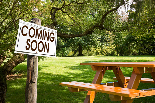 Coming soon written on a signboard near a picnic table on a green meadow - concept image