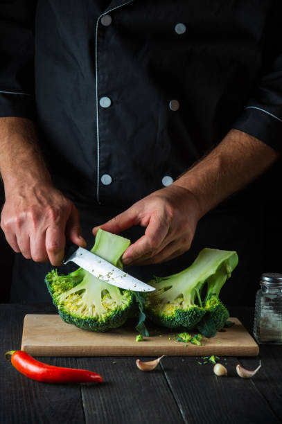 istock Professional chef cuts fresh Broccoli with a knife for salad on vintage kitchen table with fresh vegetables. Cooking and restaurant or cafe concept. 1429649348