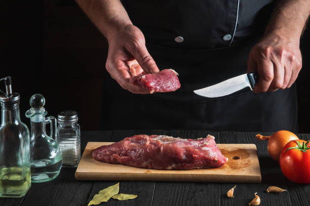 istock Chef cutting beef meat with knife on kitchen, cooking food. Vegetables and spices on kitchen table to prepare delicious lunch 1429649623