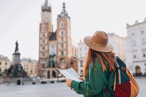 Atractiva joven turista está explorando una nueva ciudad. Chica pelirroja sosteniendo un mapa de papel en la Plaza del Mercado de Cracovia. Viajando por Europa en otoño. Basílica de Santa María photo