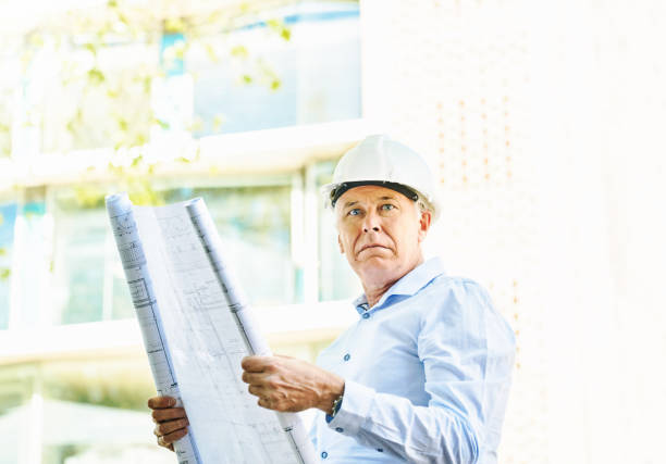 istock Handsome middle-aged man holding plans in sunshine outside a modern office building: construction boss, architect or civil engineer 1429656991
