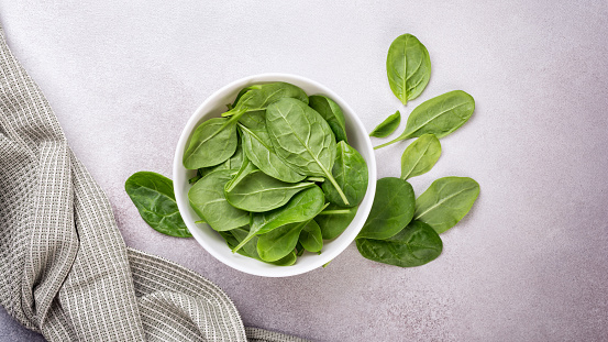 Top view of bowl with green fresh baby spinach on grey concrete background