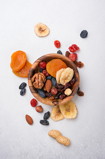 Top view of wooden bowl with dried fruit, berries and nuts as ingredient for tasty and healthy meal on grey concrete background