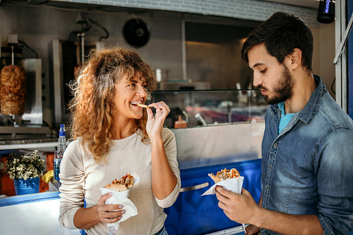 Portrait of a man and woman eating gyros in front of a fast food shop