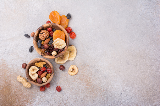 Top view of wooden bowls with dried fruit, berries and nuts as ingredient for tasty and healthy meal on grey concrete background with copy space