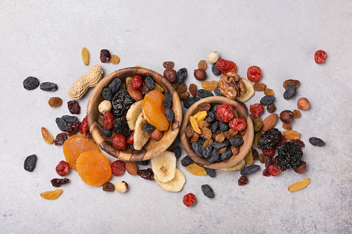 Top view of wooden bowls with dried fruit, berries and nuts as ingredient for tasty and healthy meal on grey concrete background