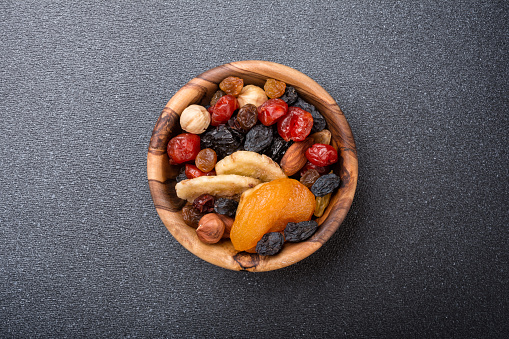 Top view of wooden bowl with dried fruit, berries and nuts as ingredient for tasty and healthy meal on dark concrete background