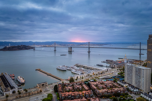 Aerial view of a sunrise behind the Bay Bridge. A burst of pink color casting a glow on the Bay.
