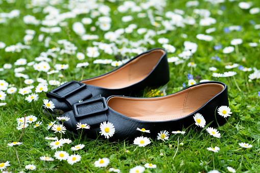 A nice black woman's shoes are on the green grassed ground, and there are white flowers