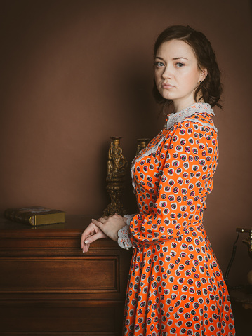 Retro-styled portrait of young attractive woman standing beside old fashioned interior