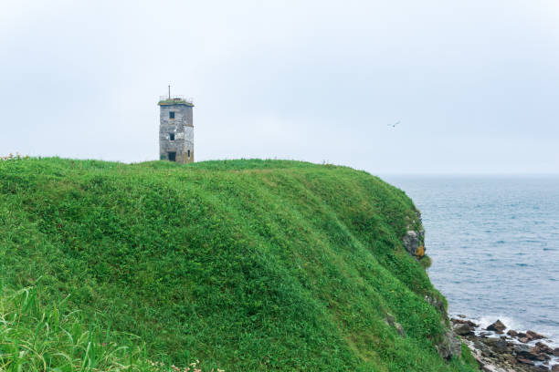 abandoned lighthouse on a high grassy promontory above a foggy sea abandoned lighthouse on a high grassy promontory above a foggy sea kunashir island stock pictures, royalty-free photos & images