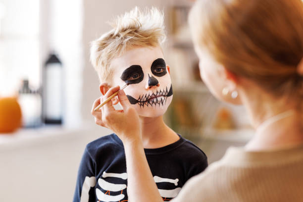 istock Festive makeup for Halloween. Woman doing skeleton make-up for boy in costume while preparing holiday 1429685760