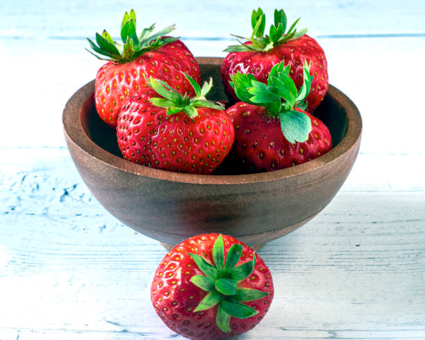 four strawberries in a bowl four fresh strawberrie in a wooden bowl with oone outside heathy snack stock pictures, royalty-free photos & images