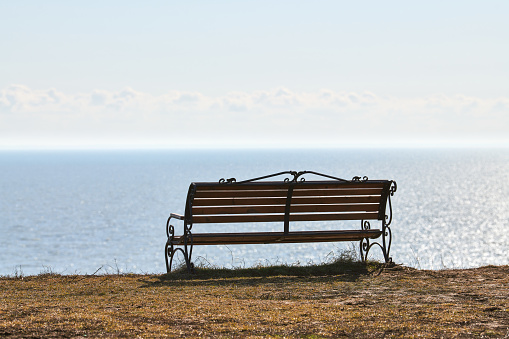 Empty bench on cliff before sea background, peaceful and quiet place for thinking alone, loneliness and loss of loved one concept. Pacifying view of marine horizon of Azov sea in Russia