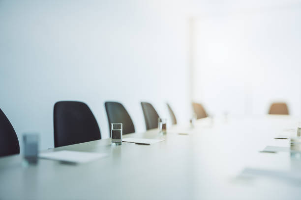 mesa de conferência leve com copos de água e folhas de papel limpas cercada por cadeiras escuras na sala de reunião com paredes brancas, de perto. renderização 3d - boardroom chairs - fotografias e filmes do acervo