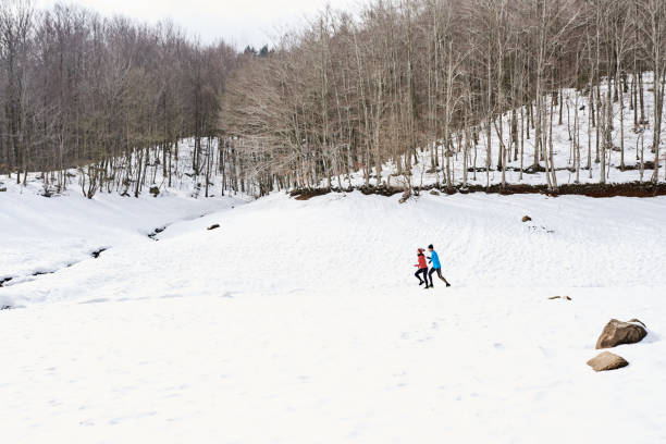 Side view of unrecognizable running couple in bright jackets on winter landscape.