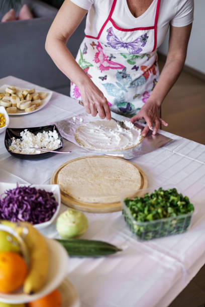 A woman is making tortillas filled with meat and vegetables.