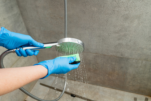 Woman in a blue glove cleans a shower head from limestone. Close-up.