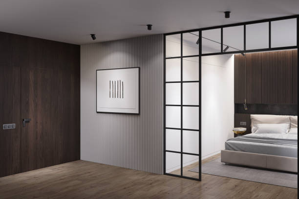 istock Dark minimalist interior with an illuminated horizontal poster on a gray wall, a built-in wooden door, a metal bedroom partition with dark wooden lockers above a light modern bed headboard. 1429700515