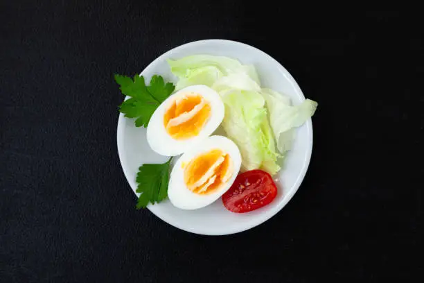 Halves of a hard-boiled chicken egg with lettuce greens on a plate on a dark background - top view