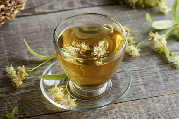 A cup of linden tea with fresh linden flowers in springtime A cup of herbal tea with fresh linden or Tilia cordata flowers on a wooden table tilia cordata stock pictures, royalty-free photos & images