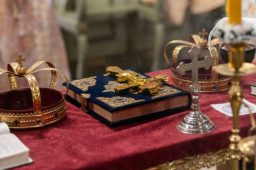 Golden church king crowns. Marriage ceremony crowns. Religious props for a orthodox Christian wedding. Table with a Bible, cross and crowns in a orthodox Christian church.