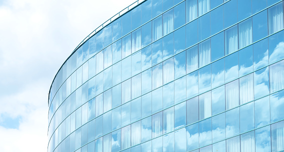 Full frame image showing the glass facade of a modern office building, with clouds reflected