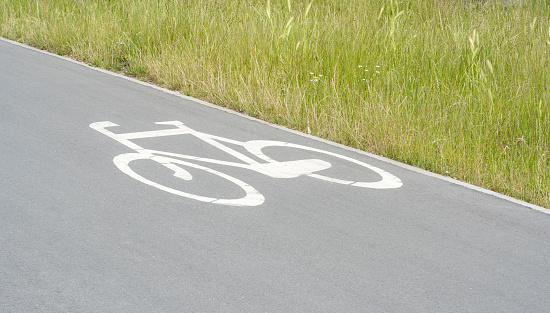 Bike lane sign on the ground, simple white bike symbol painted on the path, road, closeup detail, nobody. Cycling, biking designated areas in the city, cycle lanes infrastructure concept, no people