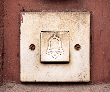 Simple old doorbell, rectangle door bell switch with a bell symbol on it, object macro, extreme closeup, front view, frontal shot, nobody, no people. Building entrance worn doorbell button up close