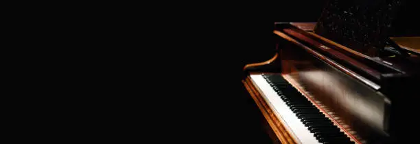 Photo of A wide photo of a real wooden classical acoustic grand piano made of wood isolated against a dark black background with copy space for a custom message