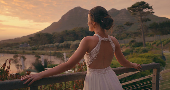 Bride in sunset after mountain wedding in countryside, woman at marriage reception in nature from behind in summer. Happy married person in landscape mountains and green environment at social event