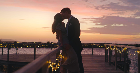 Wedding, love and couple with a kissing bride and groom at sunset with a view on their marriage day. Beautiful sky in the background of a man and woman sharing an intimate kiss after getting married