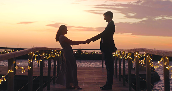 Couple silhouette at wedding with sunset, ocean and sky background for love, marriage and celebration. Man and woman or bride holding hands for trust, support and sharing life together
