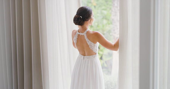 Bride at window before wedding celebration, marriage and reception from the back. Elegant beauty of a young woman in bridal fashion dress getting married for special, happy and romantic event