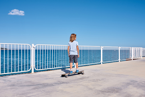 8 year old boy riding a longboard on a pier at sunny day