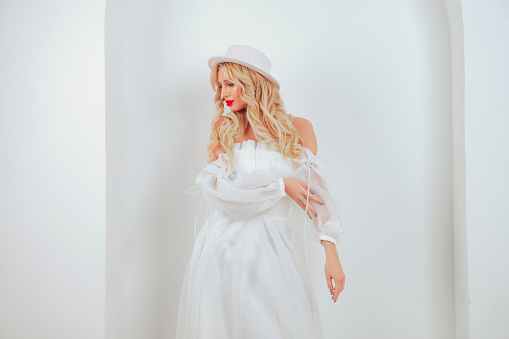 Soft portrait stylish french style bride young woman in white wedding dress and hat posing, looking away. Bride female in studio room on grey wall background. Fashion, vogue concept. Copy text space