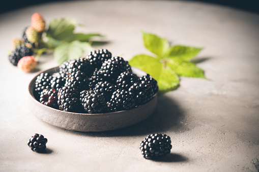 Ripe blackberries with leaves in a bowl on a dark rustic background
