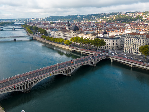 Aerial drone view of the River Rhone in the French city of Lyon, looking down at the Pont Wilson bridge. The view looks across to the historic part of the city on the north bank, which is on a peninsula of land with the Rhone on the south side and the River Saone on the north side of the peninsula. The area is part of a UNESCO World Heritage site.