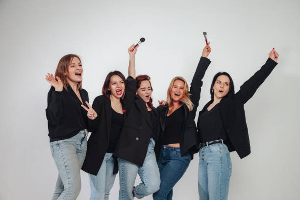 Five confident stylish adult fun women with make up brushes posing on grey wall background. Females makeup artist posing in studio. Fashion, vogue, business concept. Copy text space
