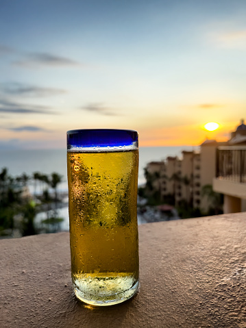Ice cold beer with typical background of the Pacific Ocean during a lovely golden sunset