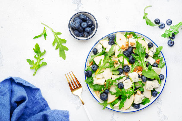 istock Tasty arugula salad with pears, blueberries, roquefort cheese and walnuts. White stone kitchen table, top view, copy space 1429776616