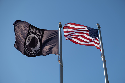 American Flag and POW-MIA flag flying in the breeze against the all blue sky