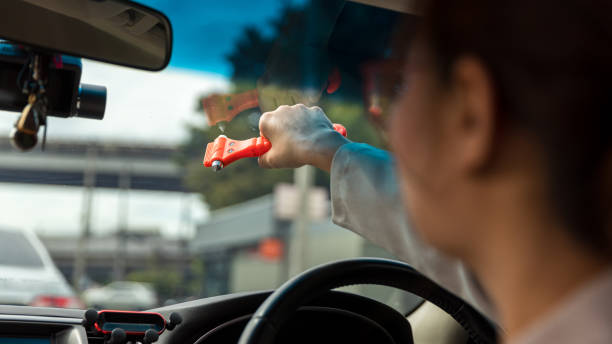 女性は車の中で安全ハンマーとシートベルトカッターを使用し、緊急時にガラスを割ります。車の安全赤いハンマーで緊急の場合は、草の窓を壊します。 - broken window glass women ストックフォトと画像
