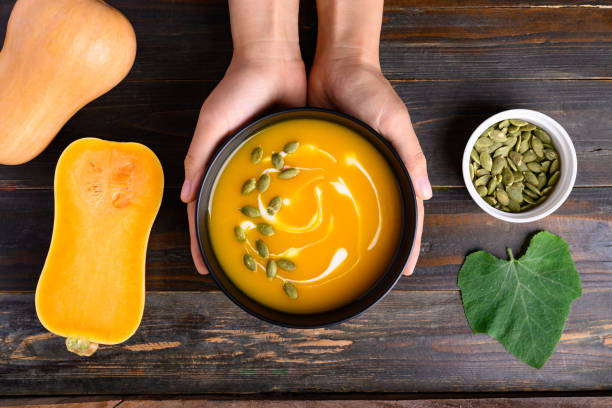 Butternut squash pumpkin soup in bowl holding by hand on wooden background stock photo