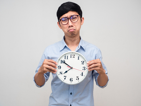 Asian businessman wear glasses holding analog clock feels boring to work isolated