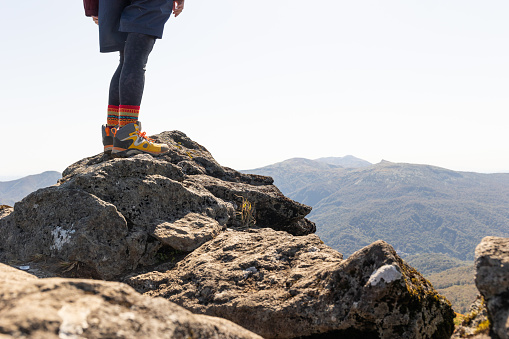 A mid tight shot of a woman standing on top of a mountain summit.
