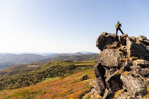 A Japanese female hiker on a rocky mountain summit looking out to the surrounding mountains and view.