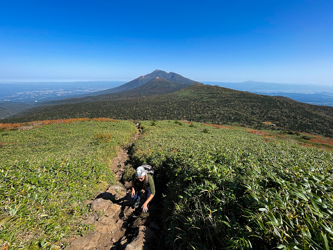 A Japanese woman solo mountain hiking along a trail with views towards Mt. Iwate in the background.