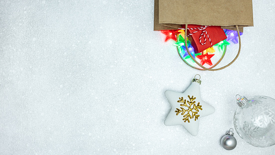 christmas star and glass balls fall out from a shopping paper bag with gift and garland lights. silver background, top view.
